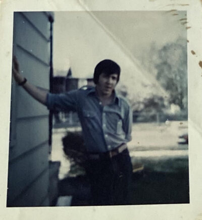 Young man leaning against a house exterior on a sunny day.